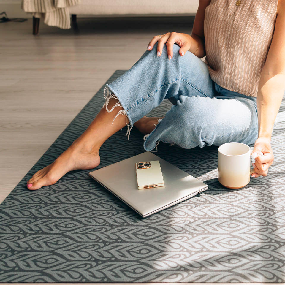 Woman sitting on the Un-Rug Color Washed Quill in her living room with her laptop, phone, and tea.