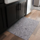 A machine washable Un-Rug in the Fine Line Floral design, size small, in a kitchen with light oak floors and black cabinet