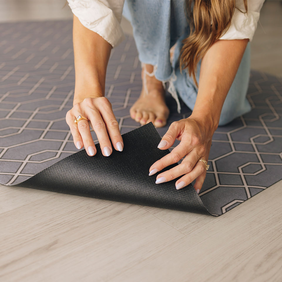 Woman flipping over the corner of a Timeless Trellis Un-Rug looking at the durable, USA made rubber backing.