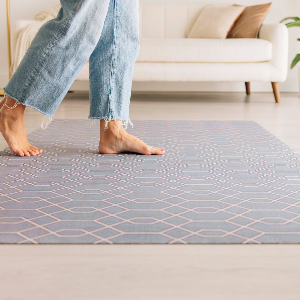 Close up of a girl walking barefoot over a low-profile Timeless Trellis mat located in a living room.