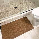 WaterHog Luxe in the circular Hourglass design in the color wheat placed perfect caddied between the entrance to a walk in shower and toilet for floor protection.