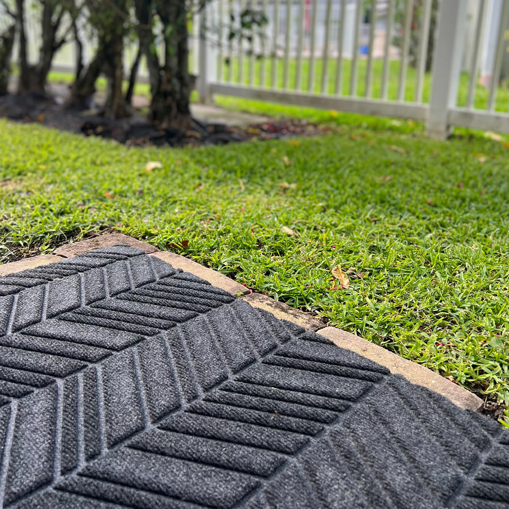 WaterHog Luxe indoor outdoor doormats placed on the edge of a patio to capture dirt, grass, leaves, and water of the bottom of boots and shoes.