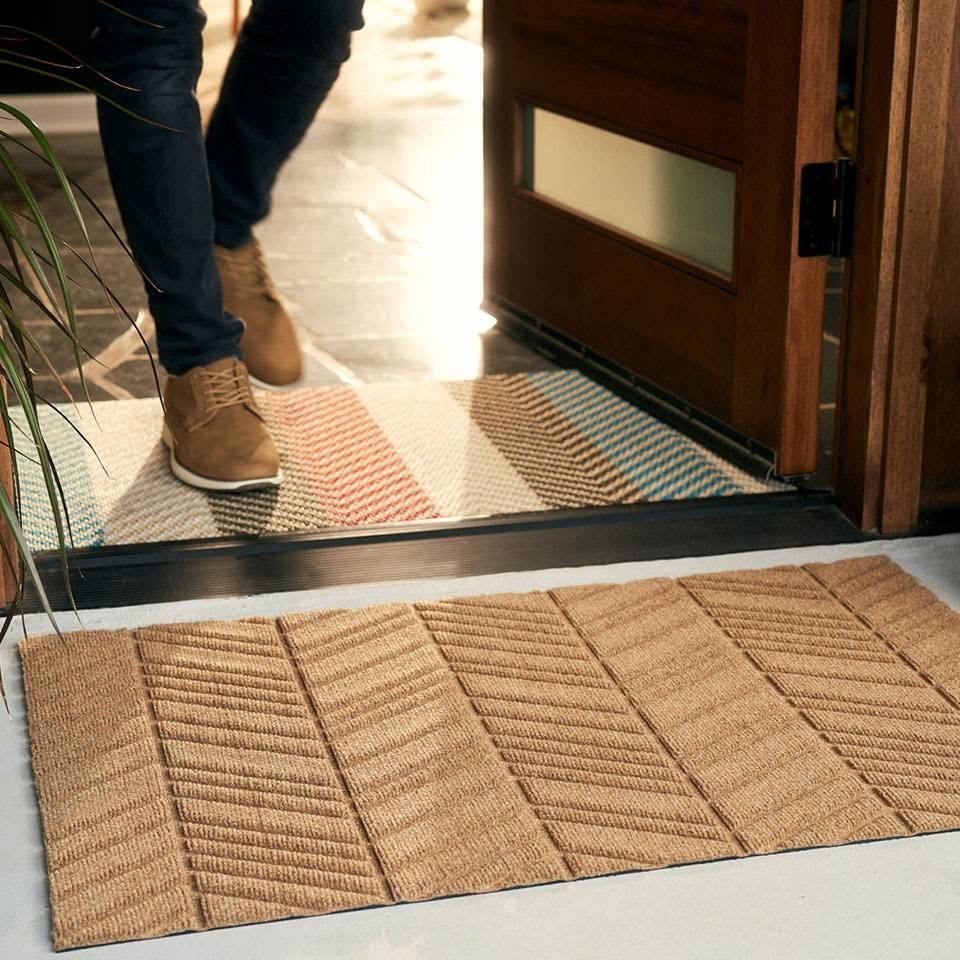 Man walking over striped multi colored doormat with wheat colored chevron bi level door outside on porch