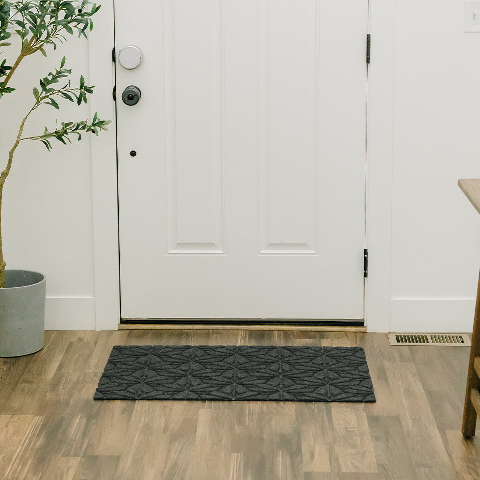 The beautiful, all-weather WaterHog Luxe Magnolia mat in graphite, located inside of a front door.