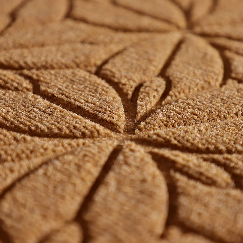 Up close, detailed image of Magnolia’s surface, capturing the floral design carved out by the bi-level surface, shown in the sandy wheat color.