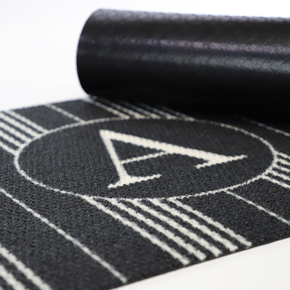 black mat with thin white stripes and monogrammed A, corner rolled over to show black rubber cleated backing