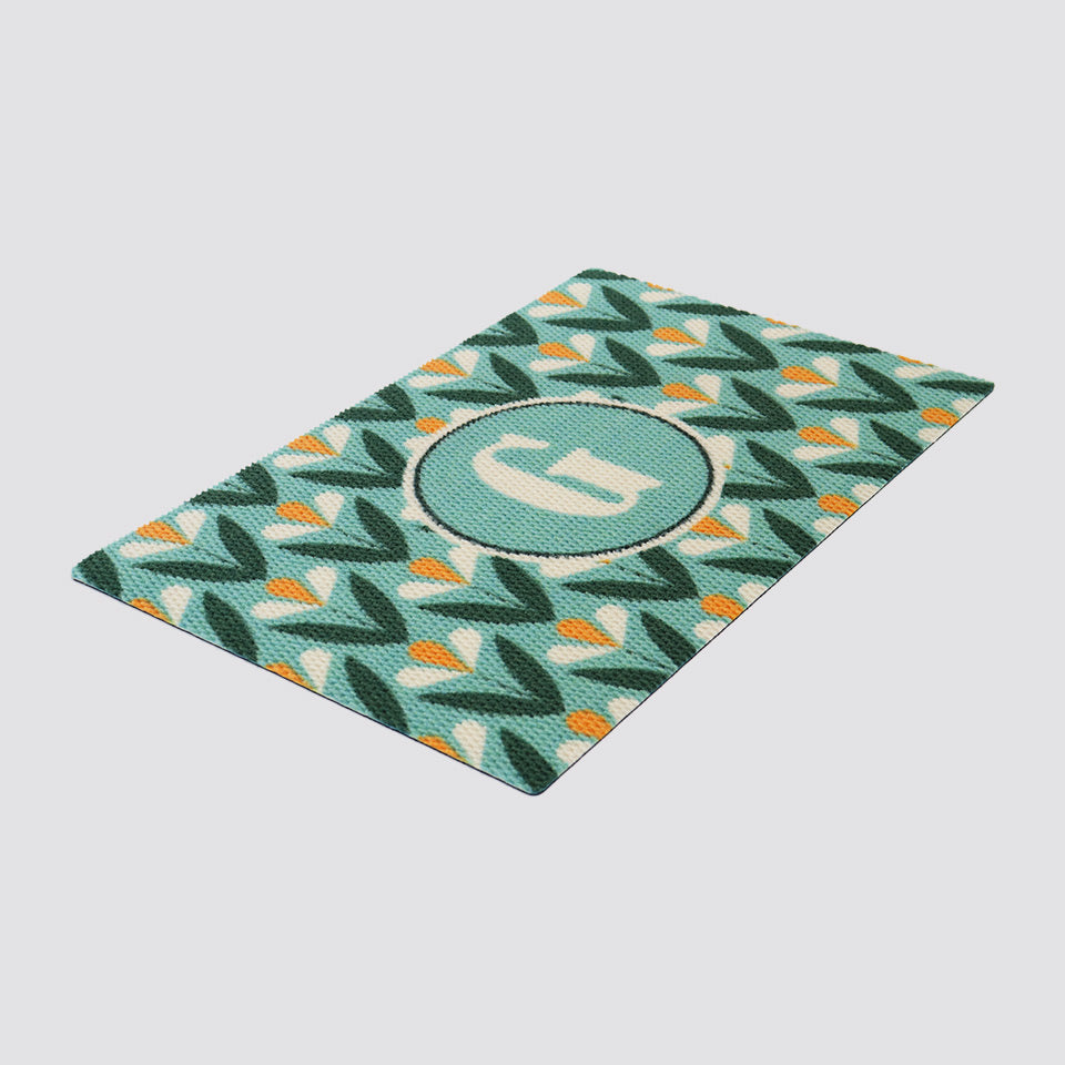 Angle shot of our MCM inspired Spring Blooms floral doormat in aqua green and yellow.  Monogrammed for a customized look to personalize your porch or entryway.  Part of our Mid Century Modern collection of doormats. 