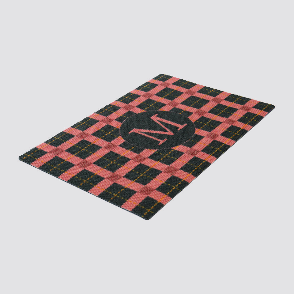 Angled shot of pink, dark grey, and gold tattersall plaid monogrammed doormat