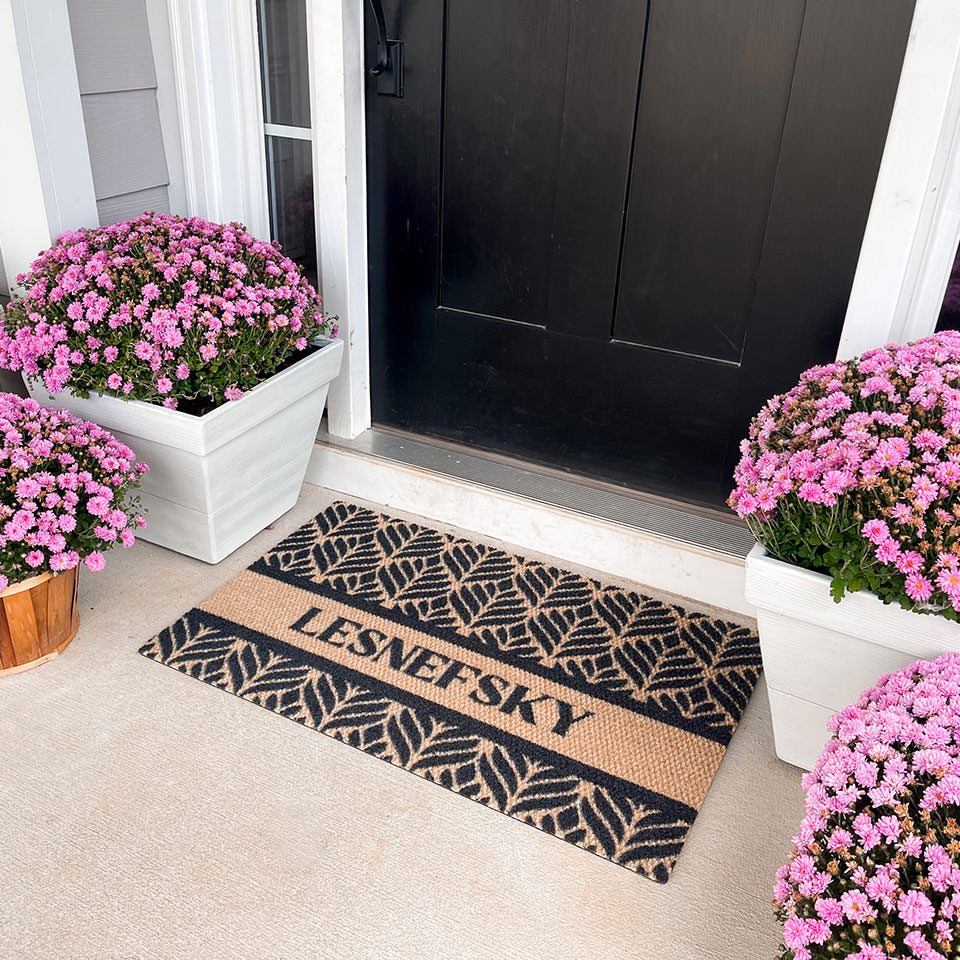single personalized botanical doormat in front of door with pink plants on either side